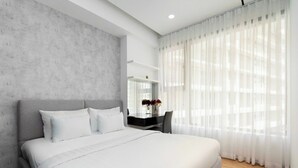 A modern hotel room with a large bed, a desk with a mirror, and sheer curtains. - Midtown Citypoint Central Suites By An Gia Hospitality (Ho Chi Minh City)