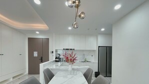 A modern kitchen with white cabinets, a marble countertop, a stainless steel refrigerator, and a dining area with a white table and grey chairs. - Midtown Citypoint Central Suites By An Gia Hospitality (Ho Chi Minh City)