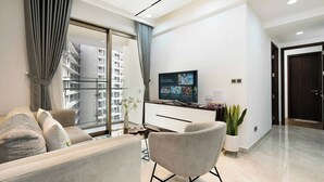A modern living room with a sofa, a chair, a TV, and a potted plant. - Midtown Citypoint Central Suites By An Gia Hospitality (Ho Chi Minh City)