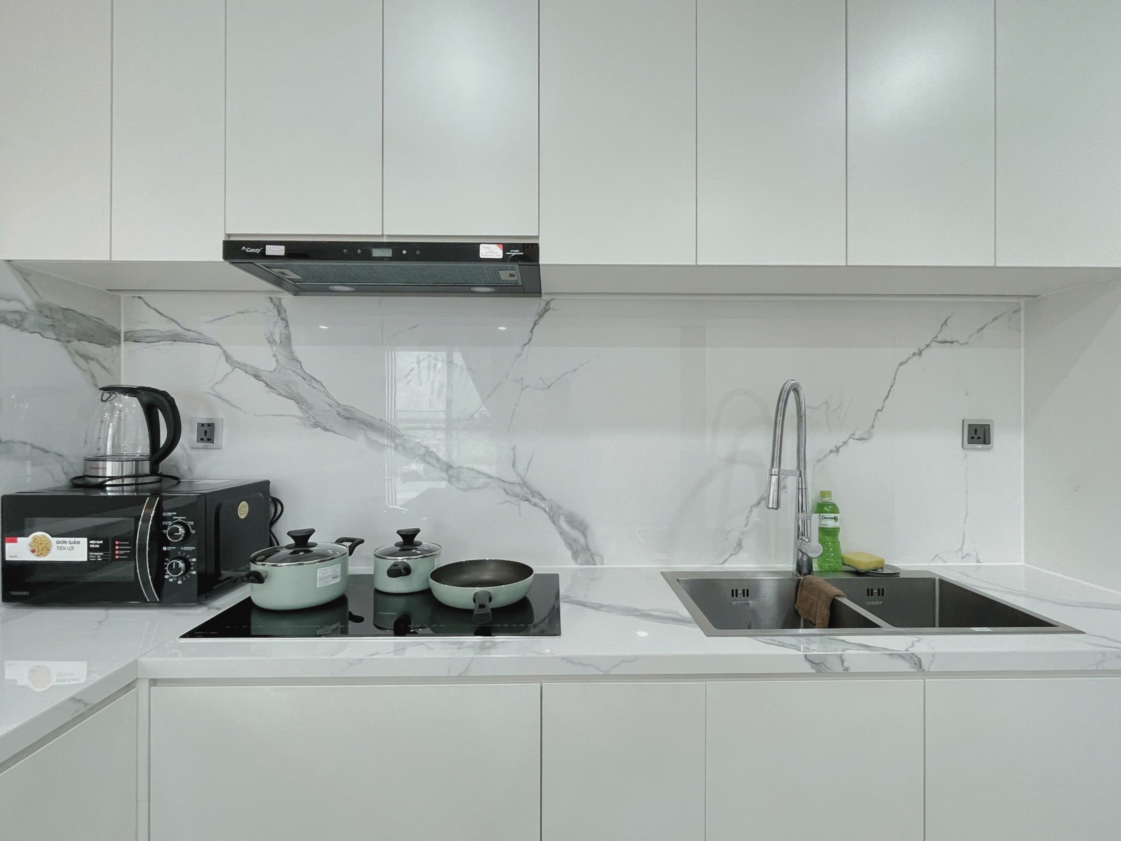 A modern kitchen with white cabinets, a built-in stove, a coffee maker, and a sink.