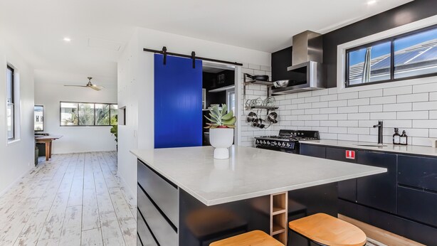 A modern kitchen with a central island, black cabinetry, and a blue accent wall. - Nestled on Nautilus (Kingscliff)