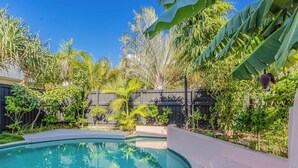 A swimming pool surrounded by lush greenery and a wooden fence. - Nestled on Nautilus (Kingscliff)