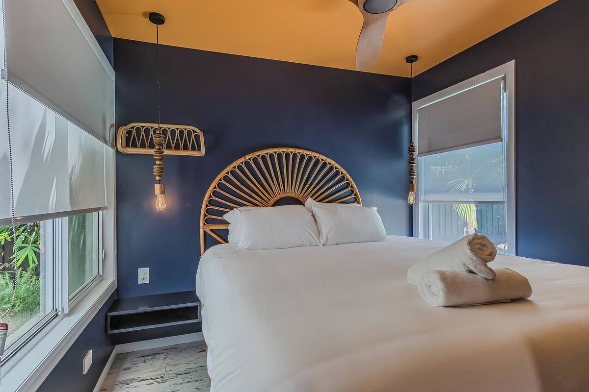 A bedroom with a bed, a unique headboard, a hanging light fixture, and a window with a view.