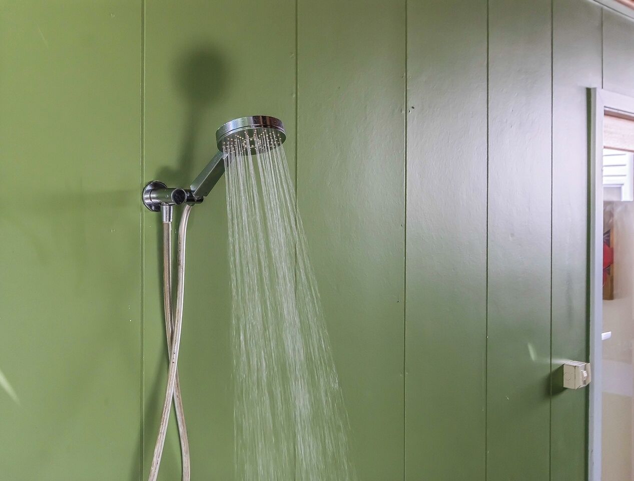 A showerhead with water flowing against a green wall.