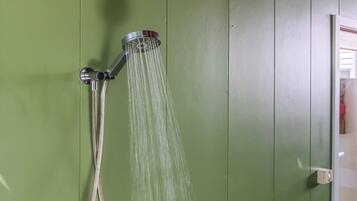 A showerhead with water flowing against a green wall.