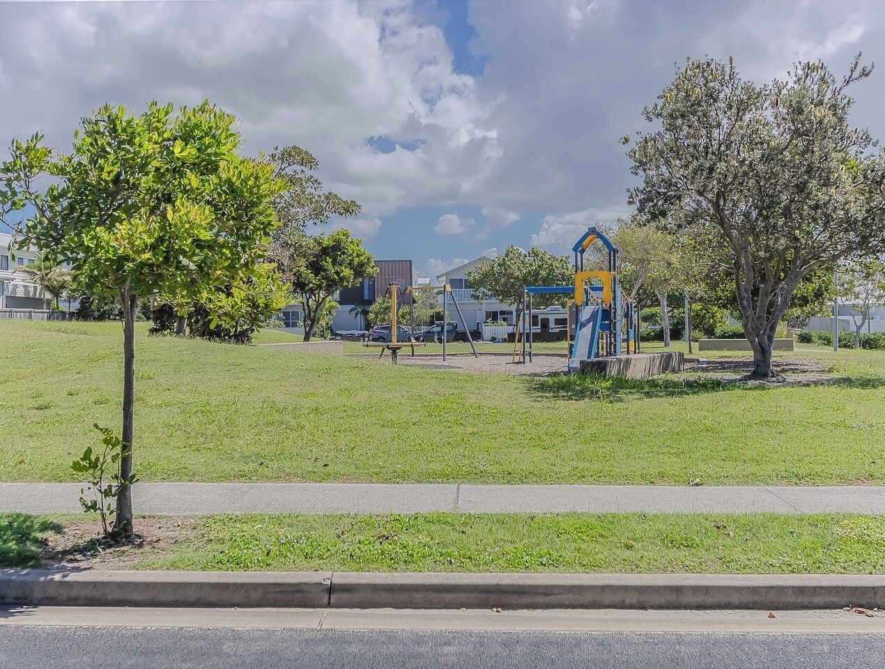 A park with a playground, trees, and a road in the foreground.