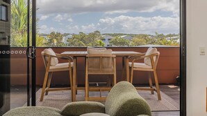 A balcony with a table and chairs, a view of the sky and trees, and a glass door. - Nestled on Nautilus (Kingscliff)