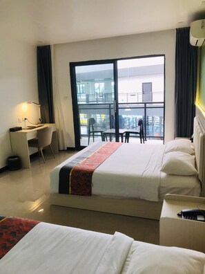 A hotel room with a bed, a desk, and a chair. There is a balcony with a view of the city.