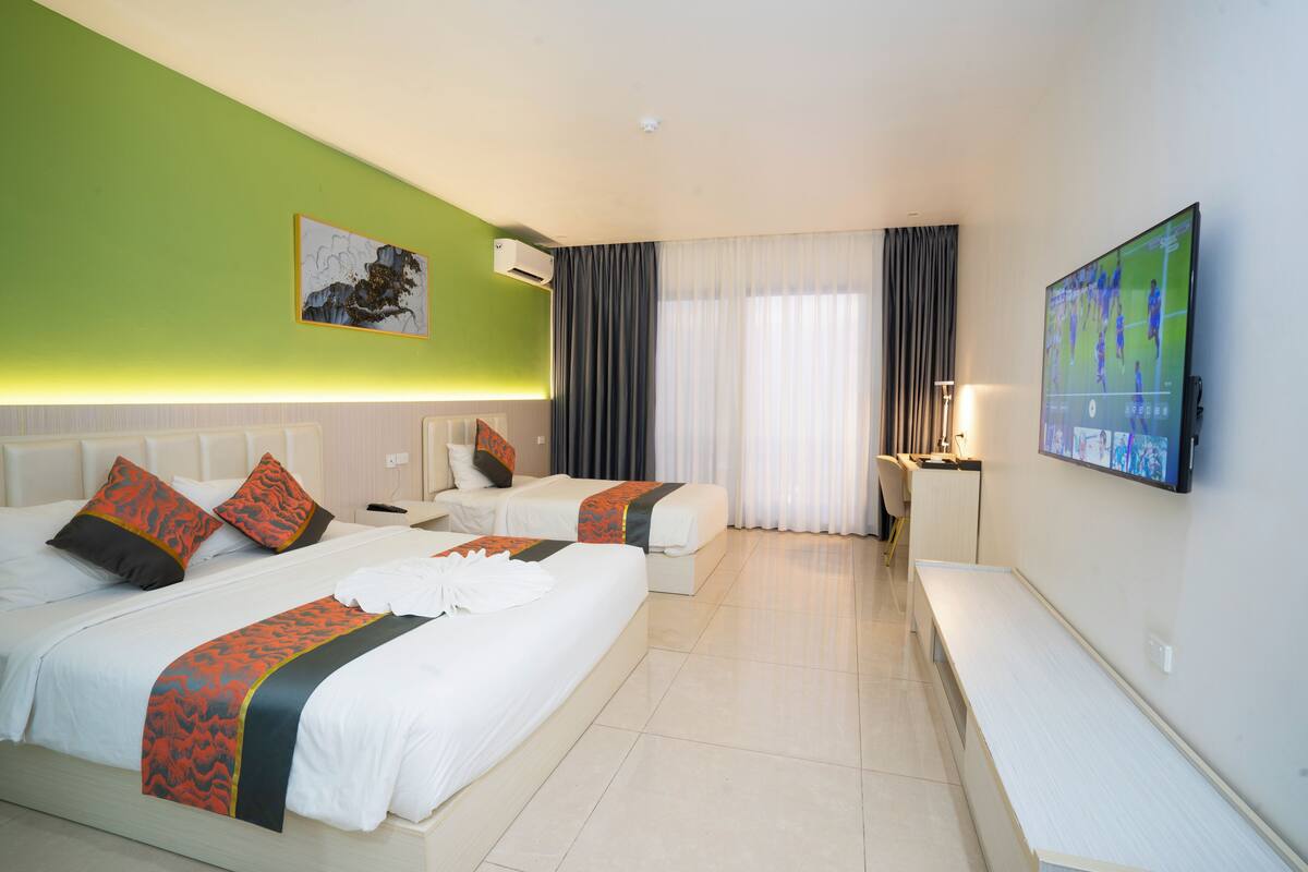 A hotel room with two beds, a flat-screen TV, a desk, and a large window with curtains.