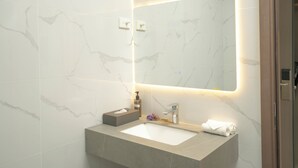 Une salle de bain avec un lavabo en marbre, un miroir doté d’un éclairage sous le meuble et un porte-serviettes.