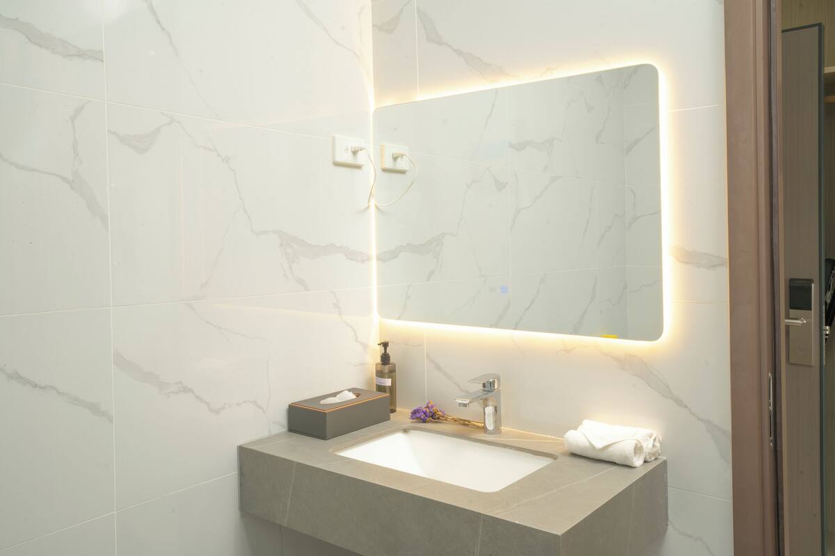 A bathroom with a marble sink, a mirror with under-cabinet lighting, and a towel rack.