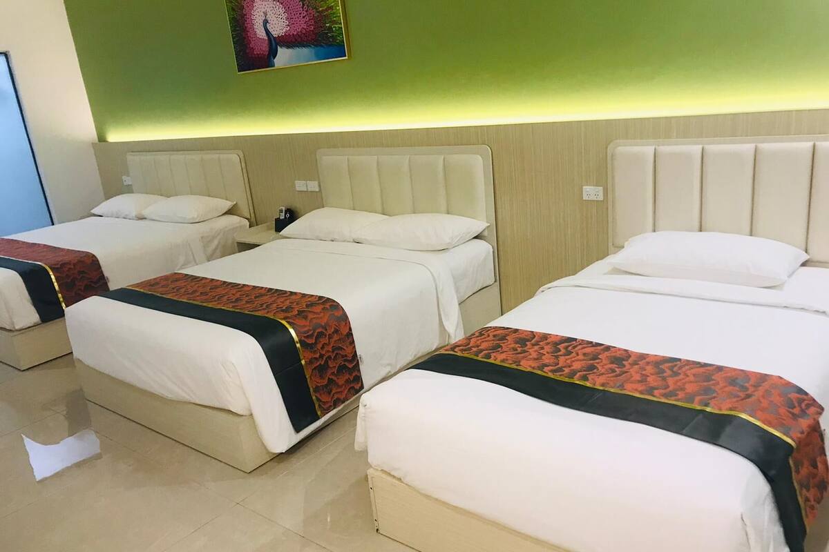 A hotel room with three beds, each with white bedding and a patterned blanket.