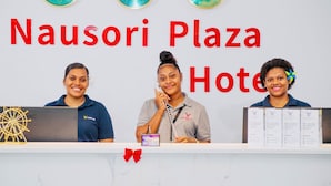 Un comptoir d’accueil à l’hôtel Nausori Plaza, avec trois employés, une horloge et une roue décorative.