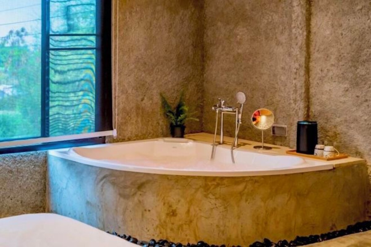 A modern bathroom with a freestanding bathtub, a small potted plant, and a coffee maker on the side.