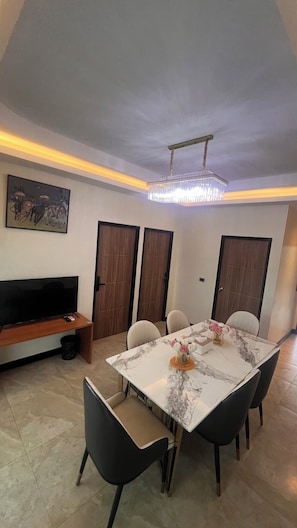 A dining area with a marble table, chairs, a chandelier, a television, and a painting on the wall.