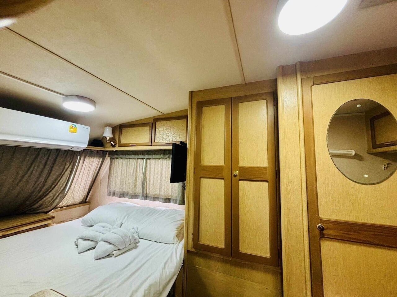 A compact bedroom with a single bed, a wardrobe, a mirror, and a ceiling fan.