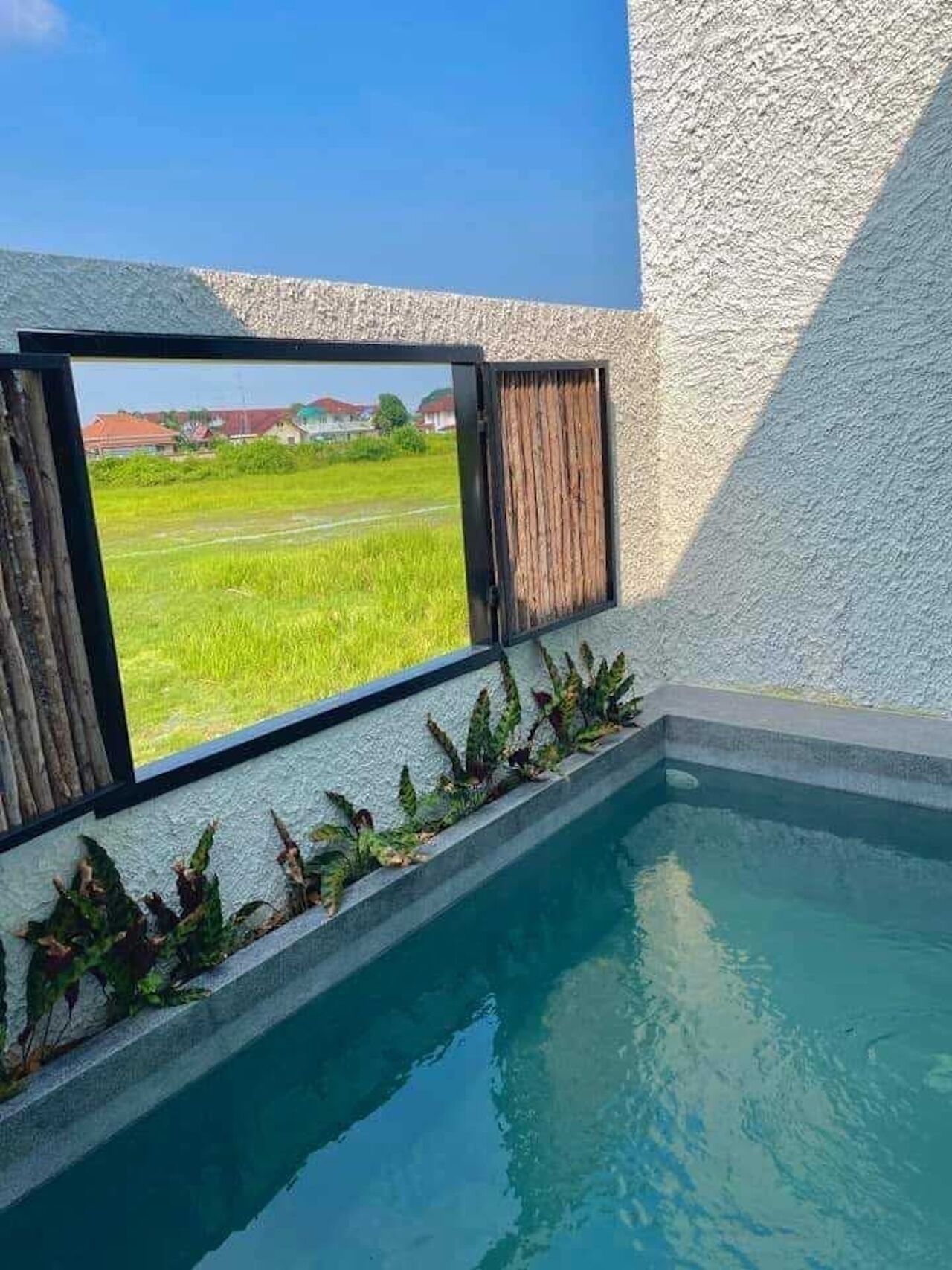 Piscina com vista para um campo verde e casas ao fundo.