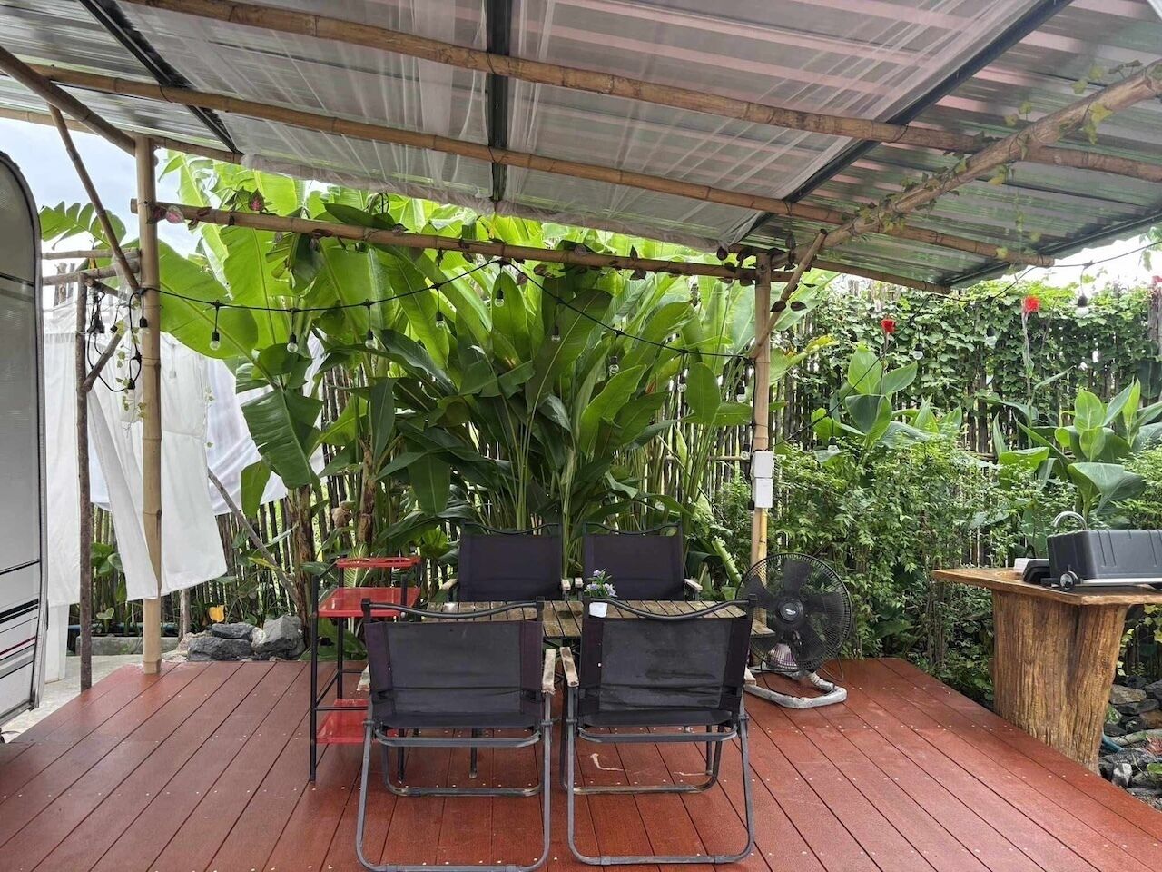 Un espacio de estar al aire libre techado con una mesa y sillas, rodeado de plantas verdes y una estructura de bambú.