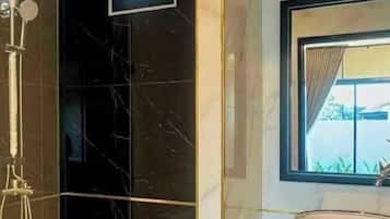 Un baño con pared de mármol negro, cabina de ducha de vidrio, espejo con marco dorado y una ventana con cortinas.