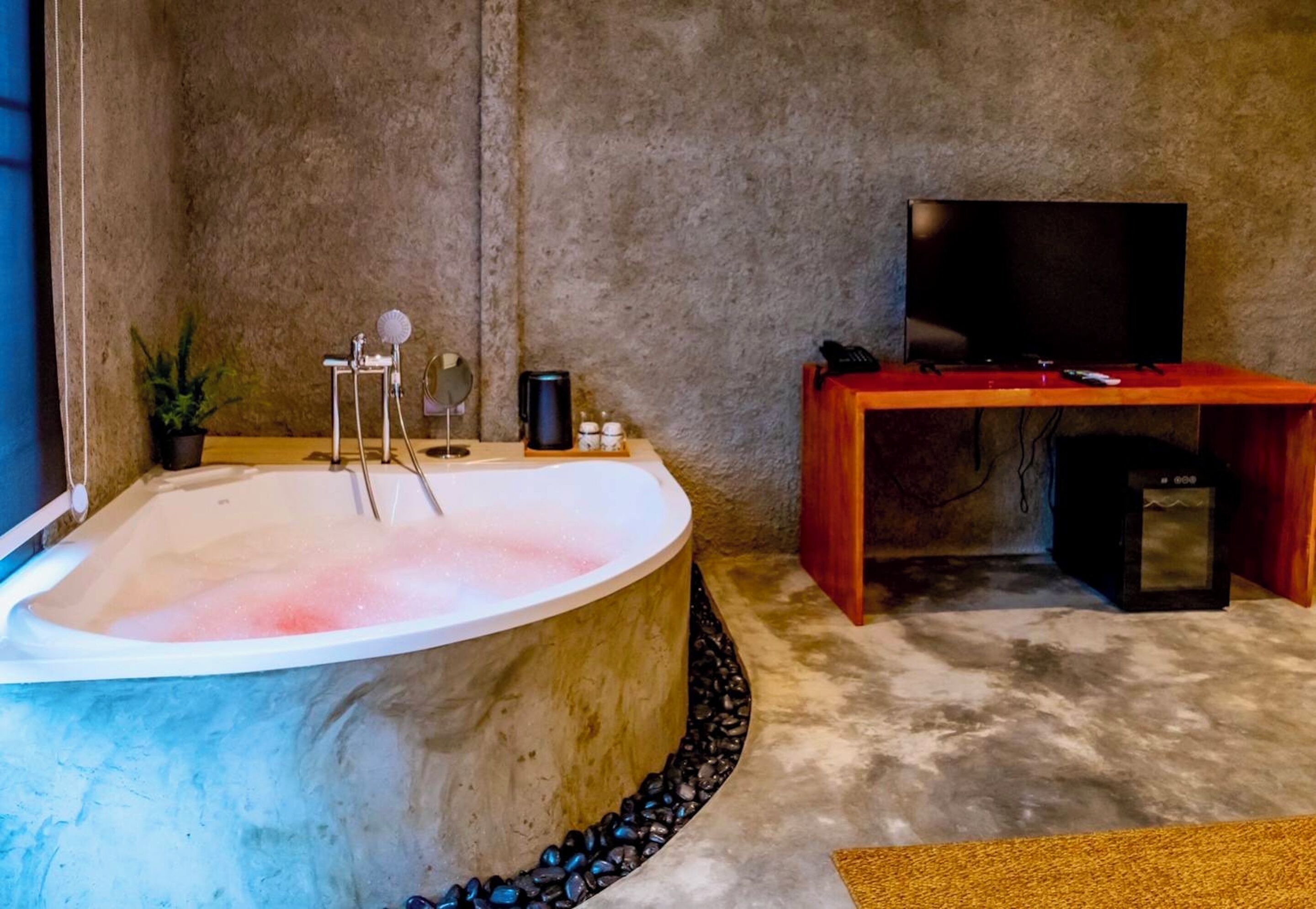 A spa room with a large bathtub, a television, and a wooden table with a remote control.