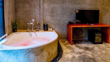 A spa room with a large bathtub, a television, and a wooden table with a remote control.