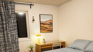 Ein Schlafzimmer mit Bett, Schreibtisch, Stuhl, Fenster und einem Bild an der Wand.