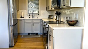 A modern kitchen with white cabinets, stainless steel appliances, and a wooden floor.
