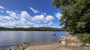 A rocky shoreline with a calm lake and a forested hill in the background.