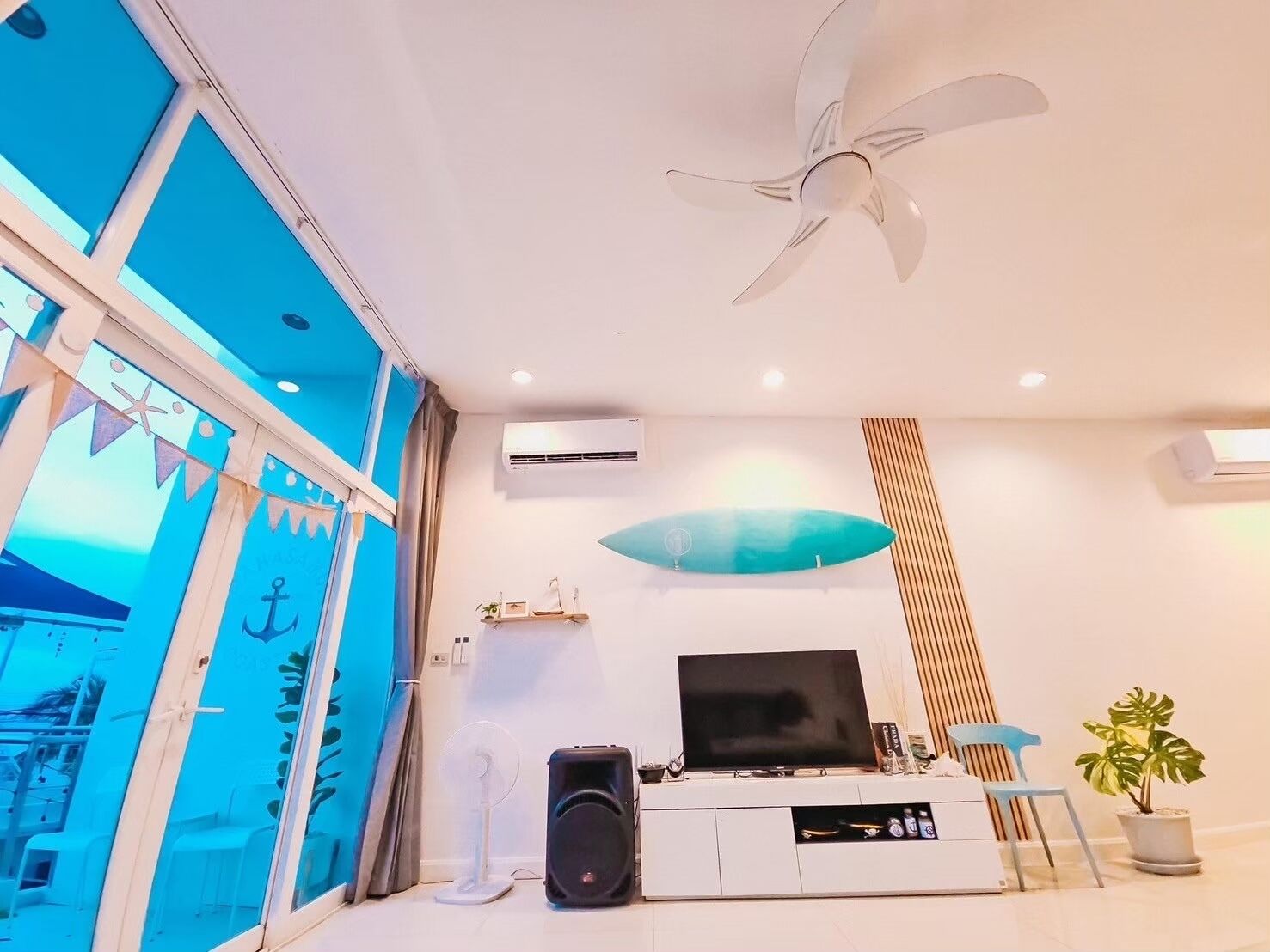 Un salon moderne doté d’un grand téléviseur à écran plat, d’un ventilateur de plafond et d’une plante en pot.