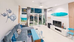 A modern living room with a grey sofa, a flat-screen TV, and a surfboard decoration. - Mahasamut coastal Poolvilla (Sattahip)
