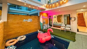 A hotel lobby with a pool area, a wooden wall with a logo, a neon sign, and a flamingo float. - Mahasamut coastal Poolvilla (Sattahip)