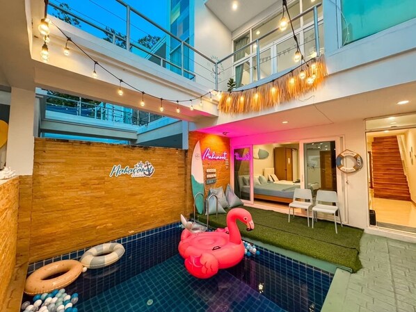 Un hall d’hôtel avec un espace piscine, un mur en bois orné d’un logo, une enseigne au néon et un flotteur en forme de flamant rose.