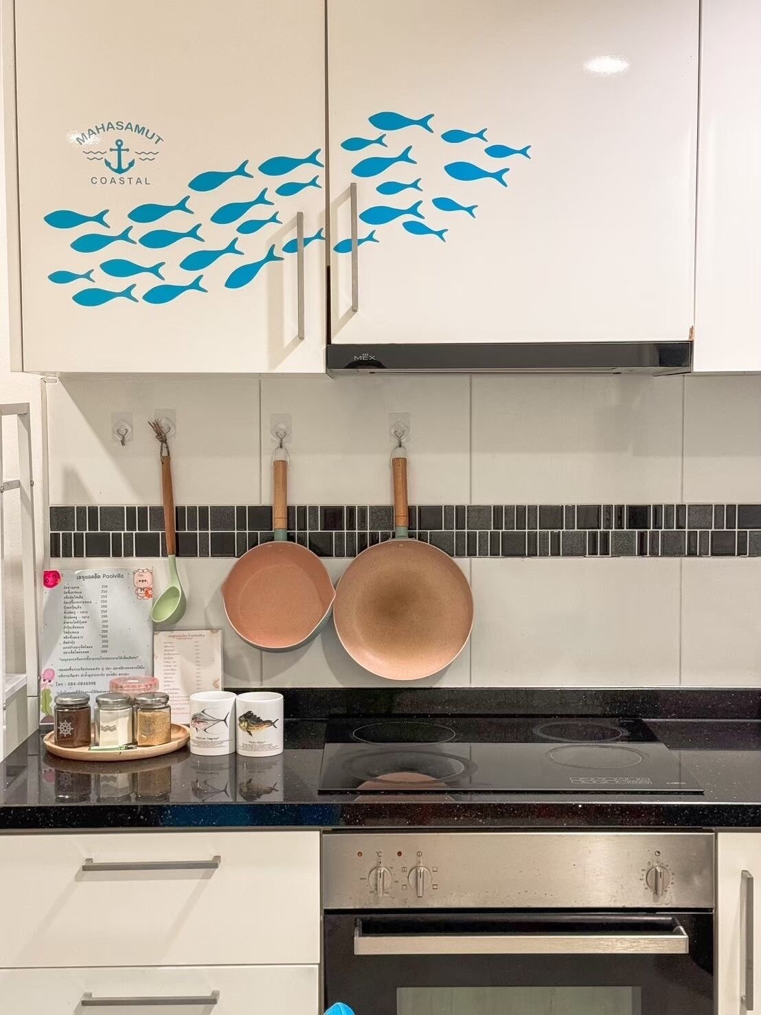 A kitchen with white cabinets, a black countertop, and a backsplash with blue fish decals.