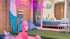 A room with a bed, a neon sign, a surfboard, and an inflatable flamingo. - Mahasamut coastal Poolvilla (Sattahip)