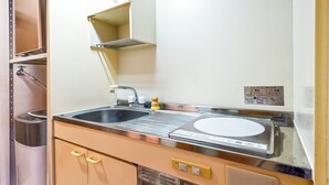 A compact kitchenette with a sink, stove, and storage cabinets. - Fukuoka Loft 303 (Fukuoka)