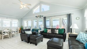 A spacious living room with a high ceiling, large windows, and a dining area with white furniture.