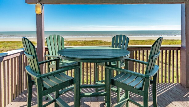 A wooden deck with a table and four chairs, overlooking a beach.