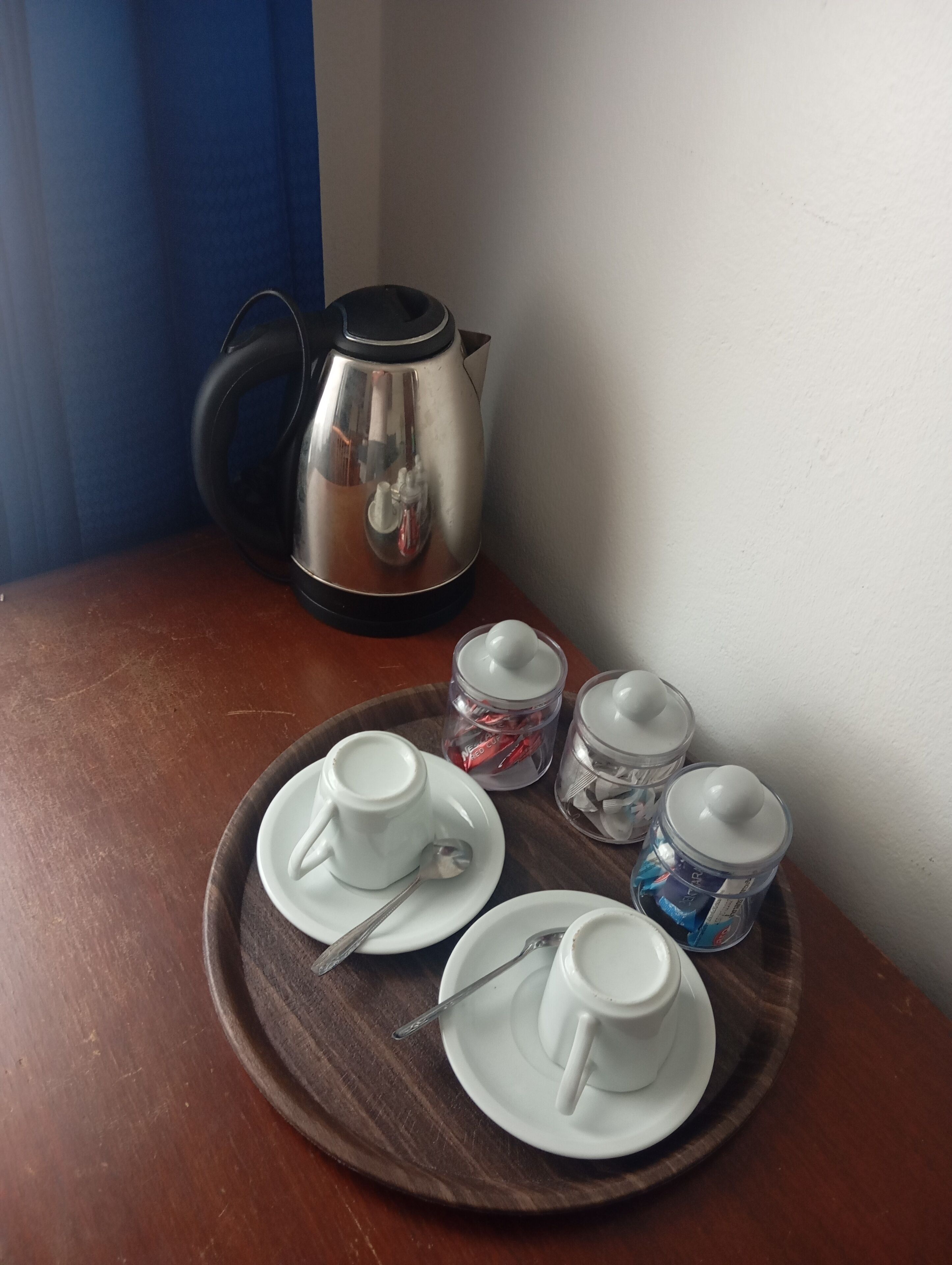 A tray with two white cups and saucers, a spoon, and two glass containers with lids on a wooden table.