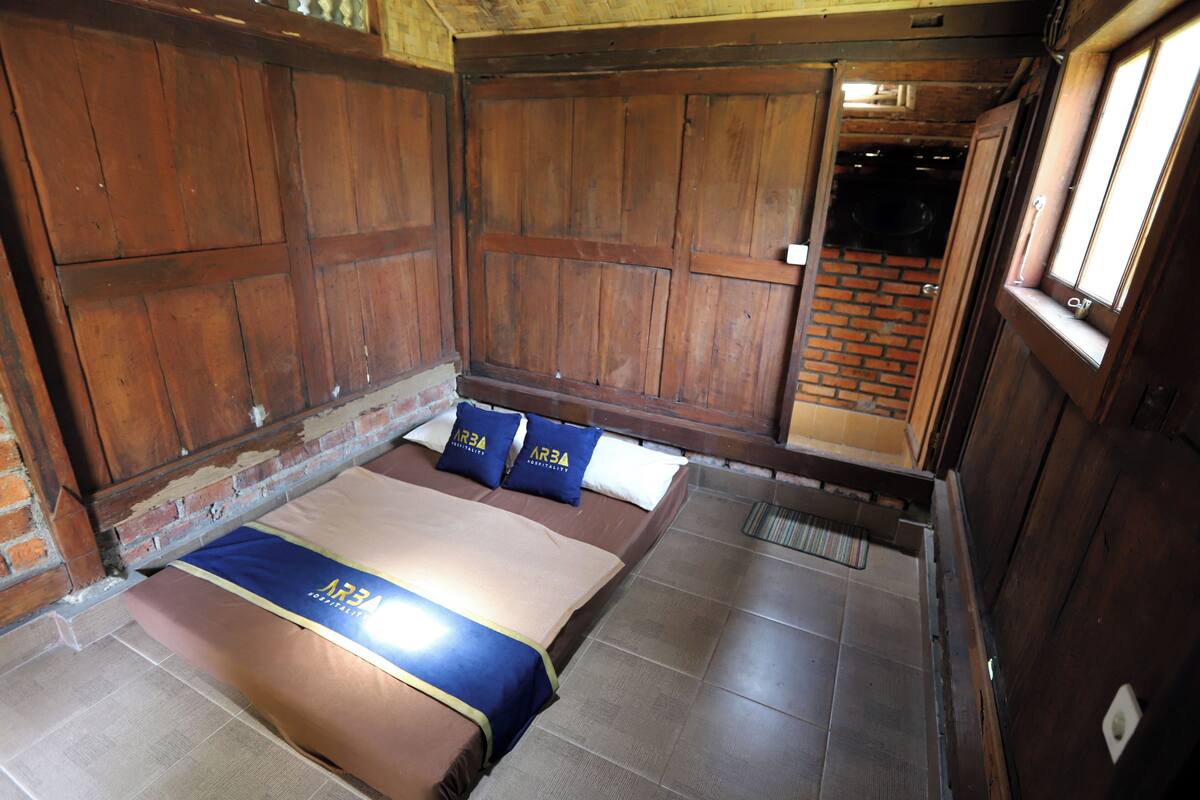 A room with a bed, wooden walls, and a brick wall.