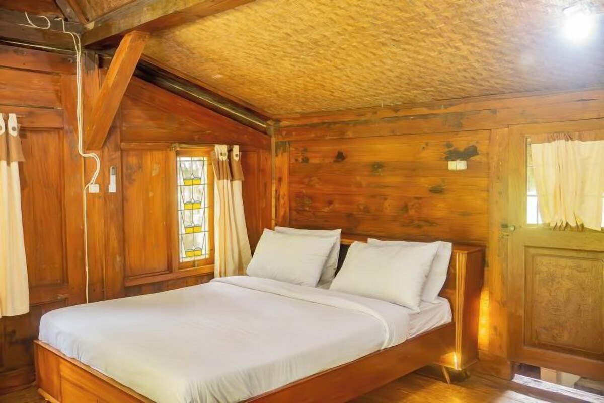 A wooden cabin-style room with a bed, wooden walls, and a sloped ceiling.