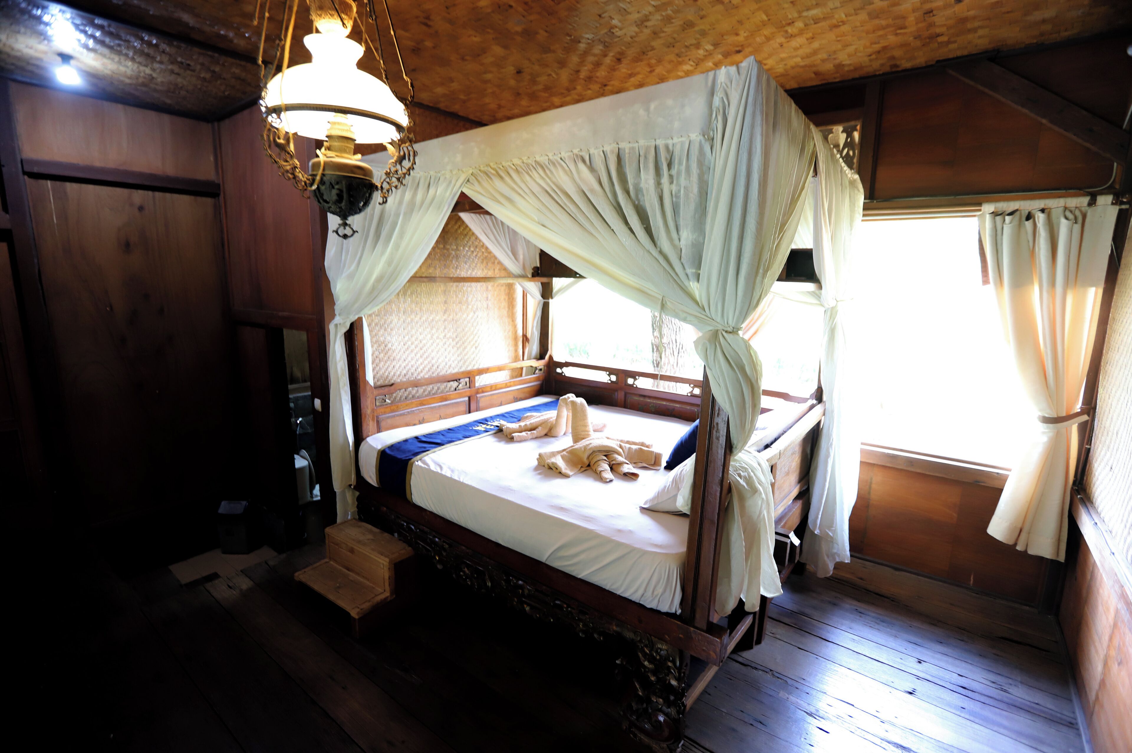 Une pièce en bois avec un lit, un luminaire suspendu et une fenêtre avec des rideaux.