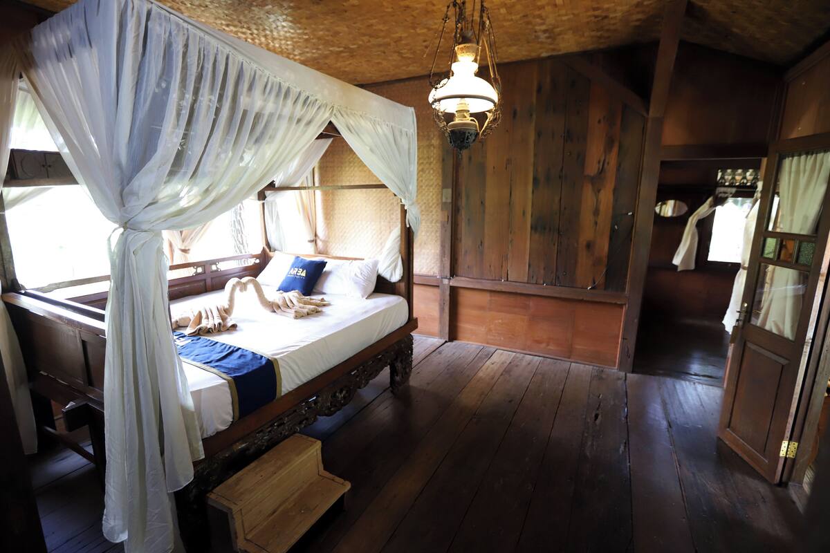A wooden room with a bed, a hanging light fixture, and a wooden door.