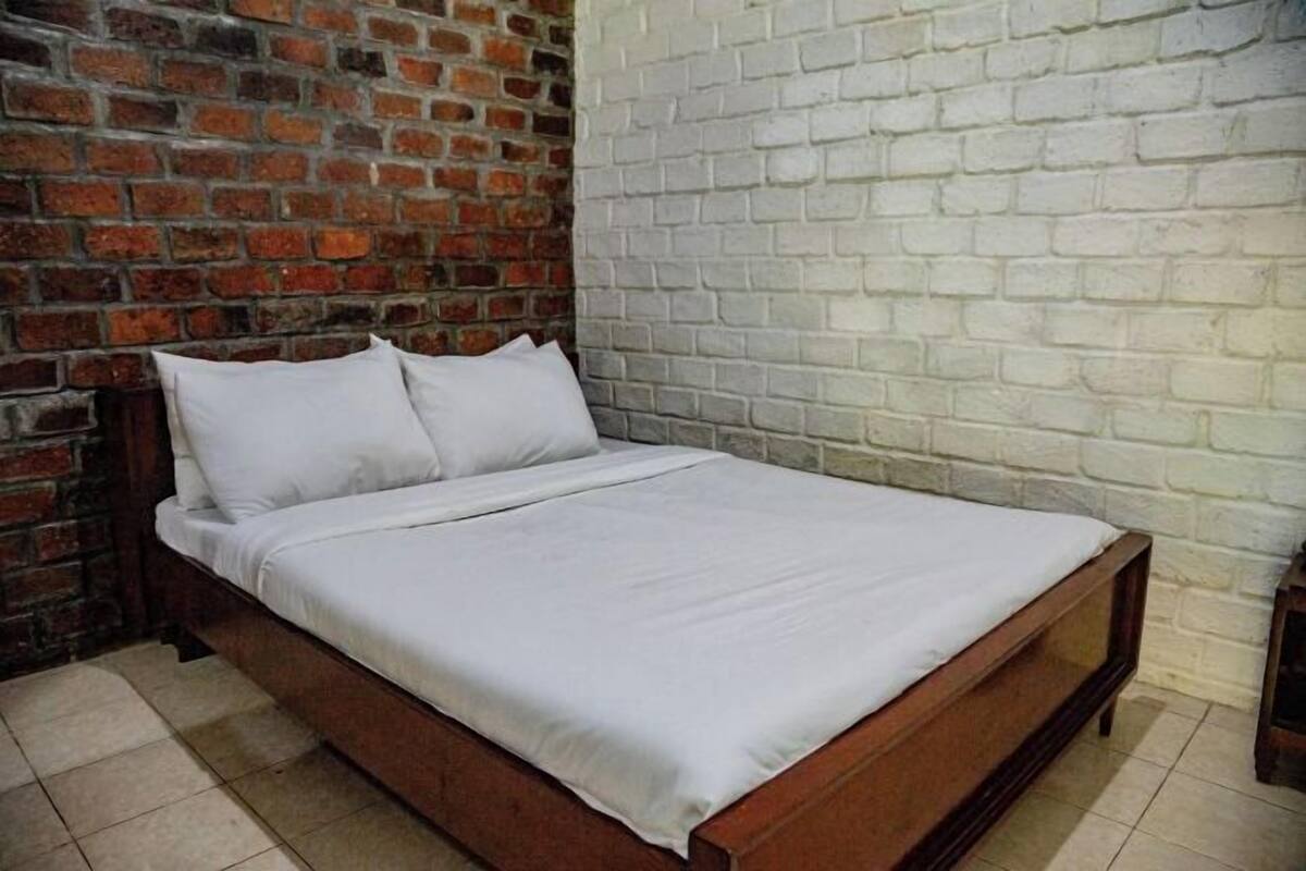 A single bed with white bedding in a room with a brick wall and a white brick wall.