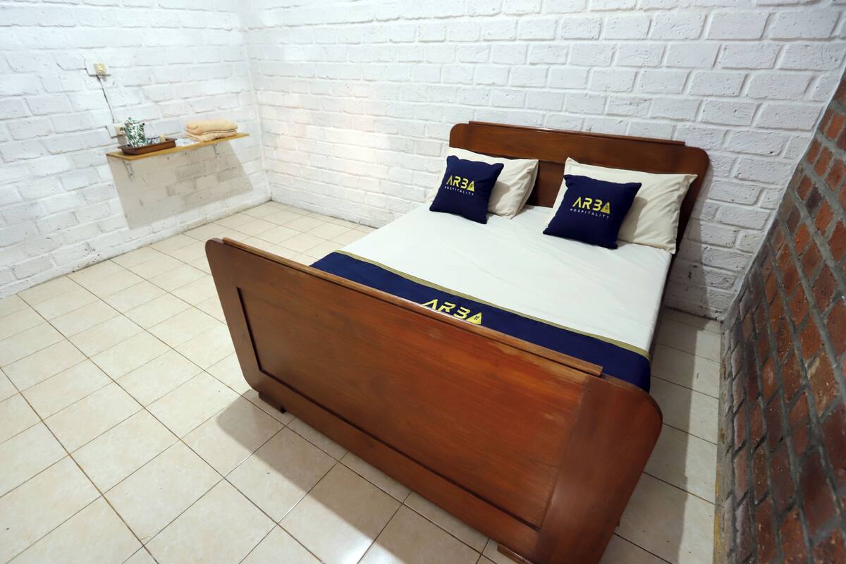 A bed with a wooden headboard, a white brick wall, and a shelf with a plant and towels.