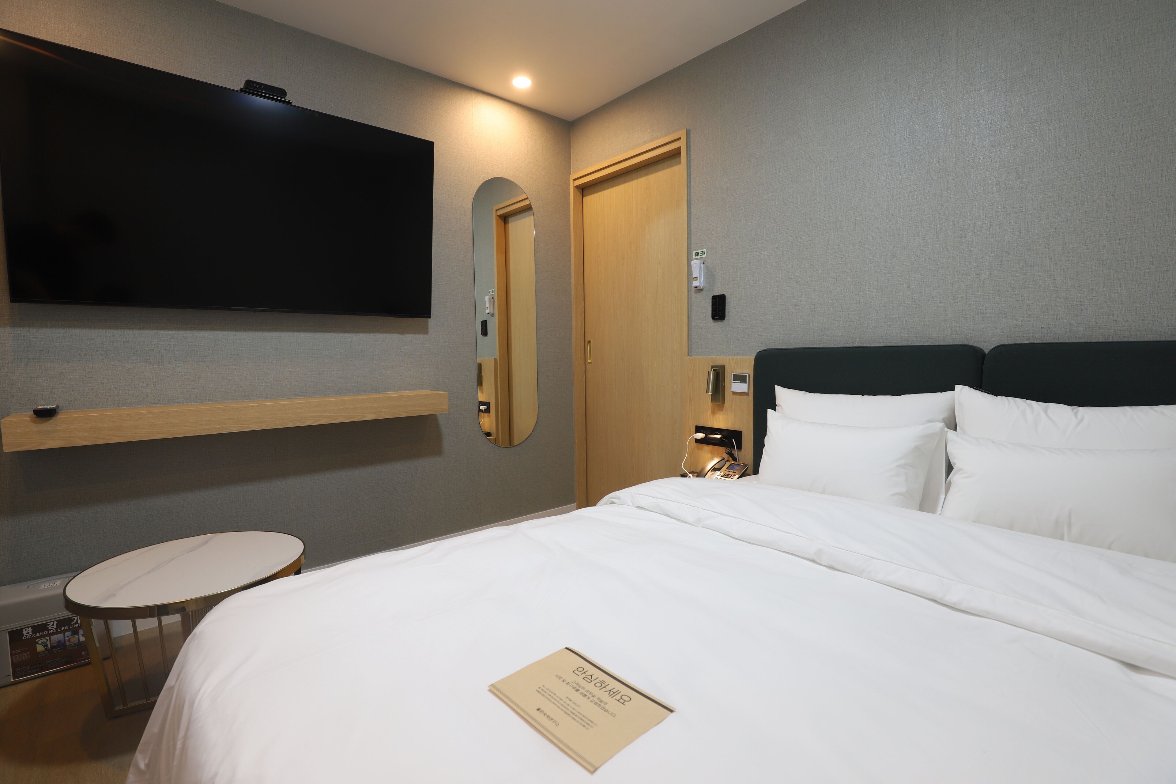 Une chambre d’hôtel avec un lit, un téléviseur fixé au mur, une table de chevet et un miroir.