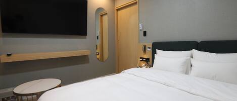A hotel room with a bed, a TV mounted on the wall, a bedside table, and a mirror.