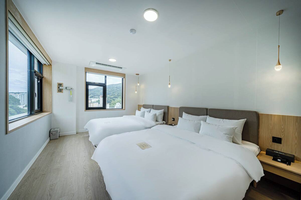 A hotel room with two beds, a window with a city view, and a small bedside table with a lamp.