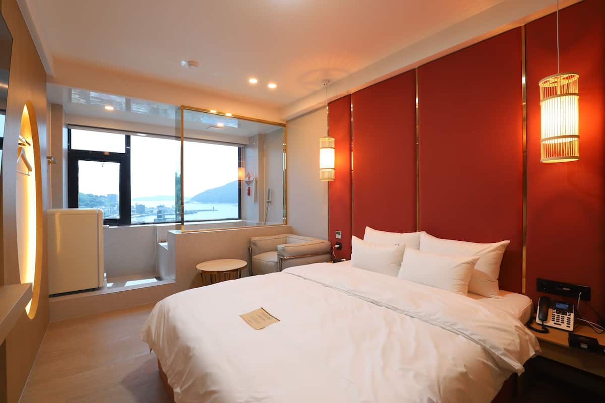 A hotel room with a large bed, a small seating area, a window with a view, and a telephone on the nightstand.