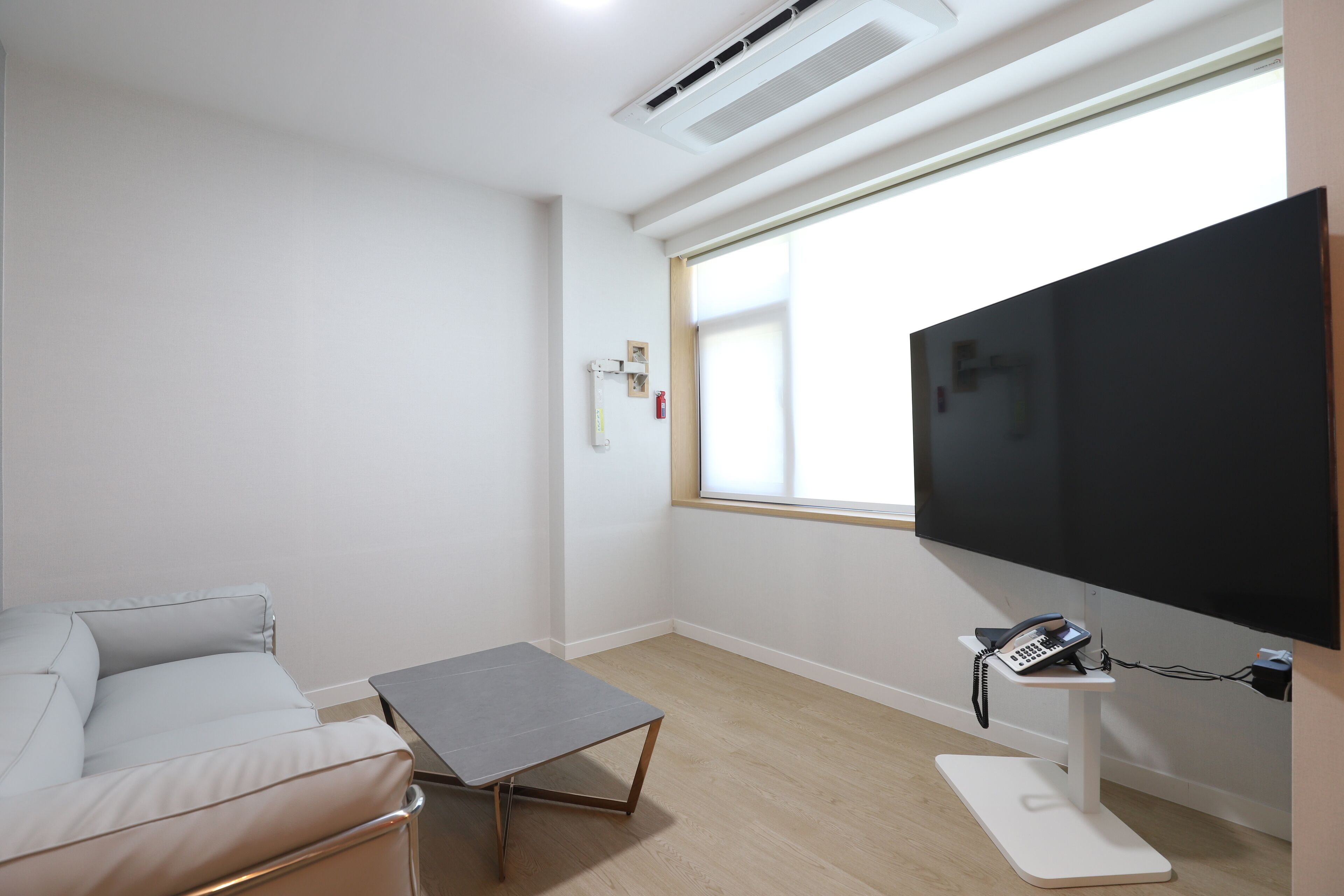 Una sala de estar moderna con un televisor de pantalla plana montado en la pared, una mesa de centro gris, un sofá blanco y una pequeña mesa blanca con un teléfono.