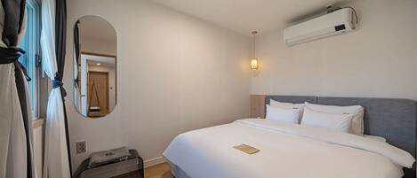 A hotel room with a bed, a bedside table, a mirror, and an air conditioning unit.